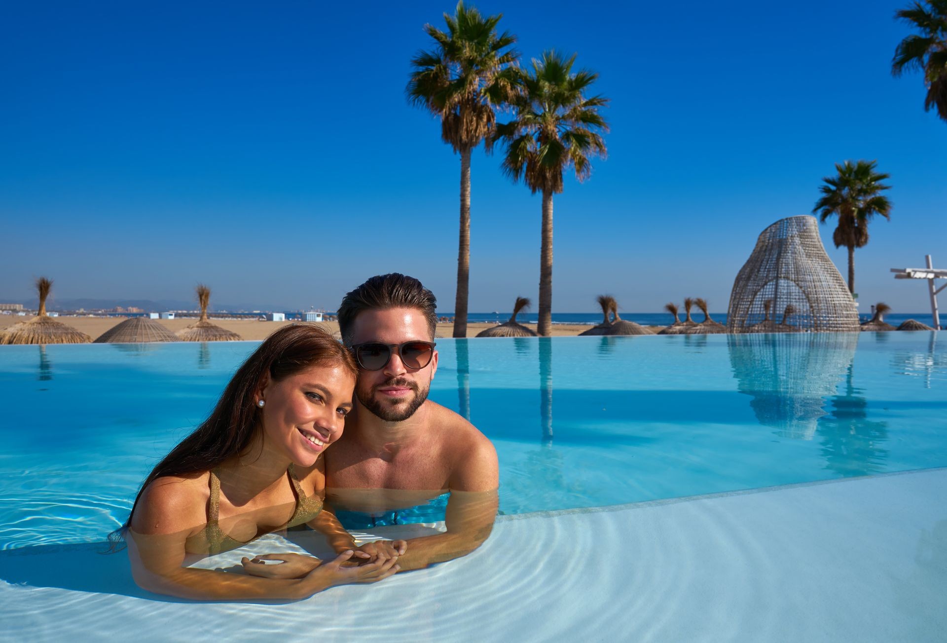 Tourist couple having bath in infinity pool on a beach resort in summer vacation